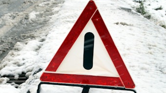 Ein Warndreieck steht in Eis und Schnee am Straßenrand.