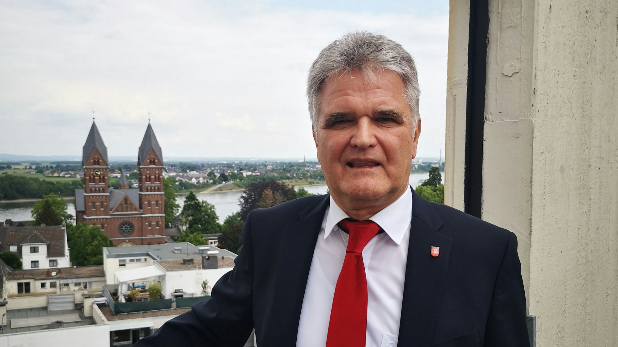Erwin Esser in schwarzem Anzug und roter Krawatte. Im Hintergrund ist die Stadt Wesseling zu sehen.