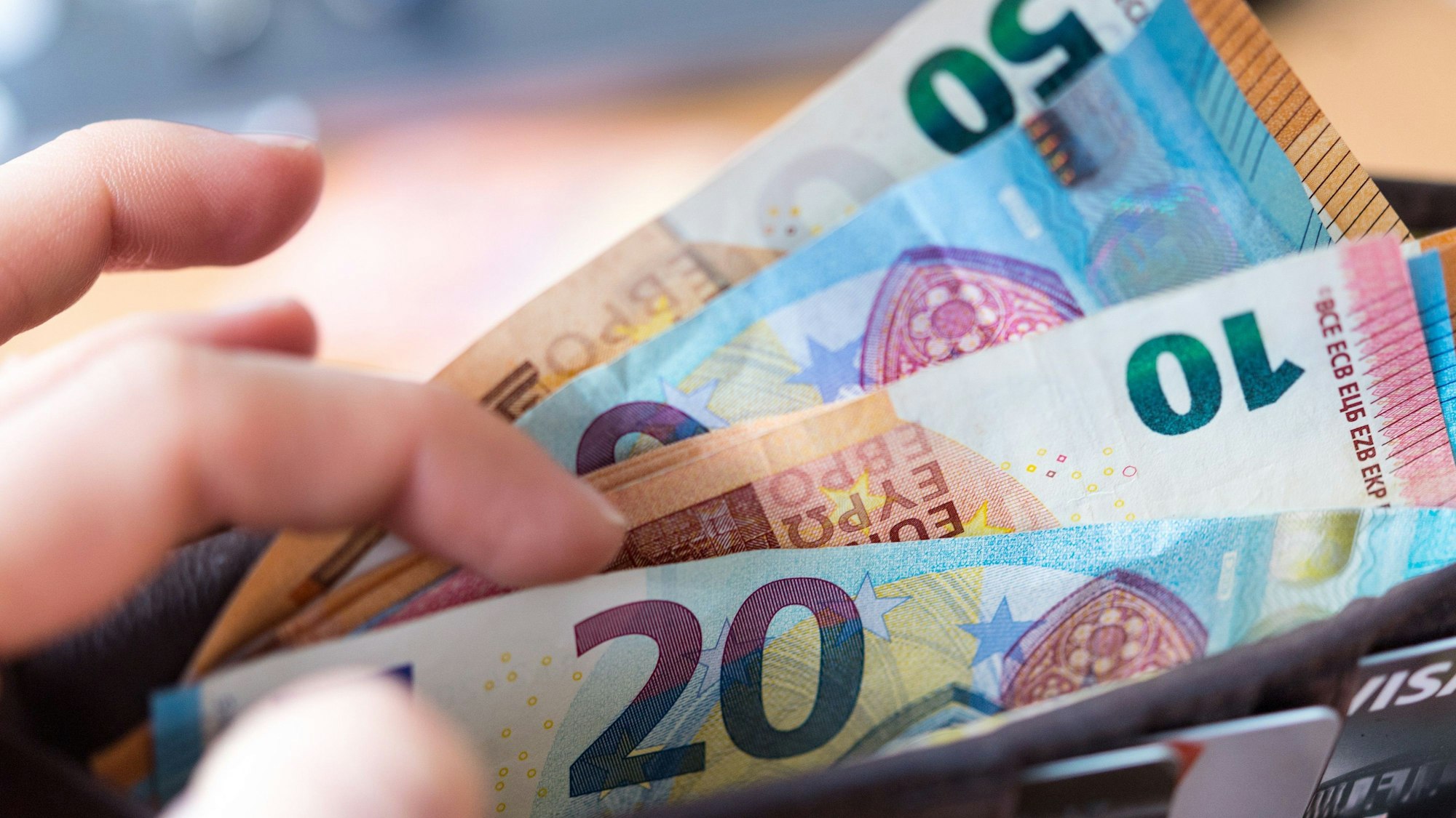 Eine Frau hält eine Geldbörse mit Banknoten in der Hand. 2022 soll es doch mehr Einnahmen in NRW geben, als bisher angenommen.