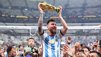 Lionel Messi hält den Weltmeisterpokal in den Händen und wird bejubelt.