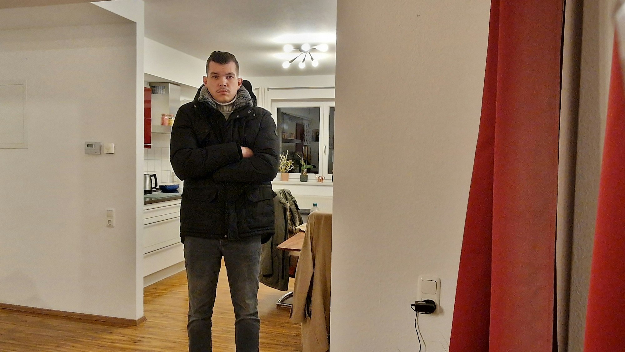 Adrian Rauhut steht in seiner Wohnung in Köln-Niehl und trägt eine Winterjacke.
