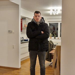 Adrian Rauhut steht in seiner Wohnung in Köln-Niehl und trägt eine Winterjacke.
