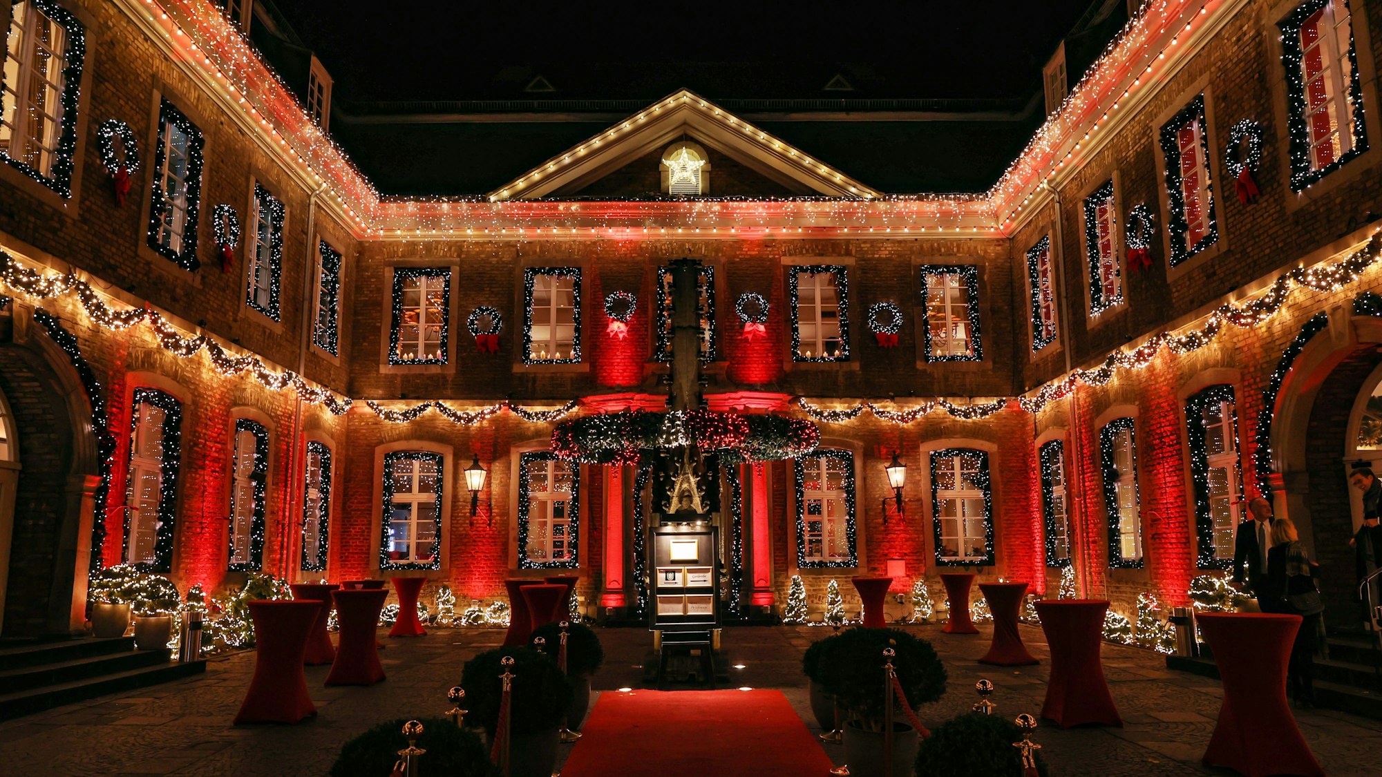 Der Innenhof der Wolkenburg ist mit zahlreichen Lichterketten sowie roten Scheinwerfern beleuchtet. An allen Fenstern hängen Girlanden.




