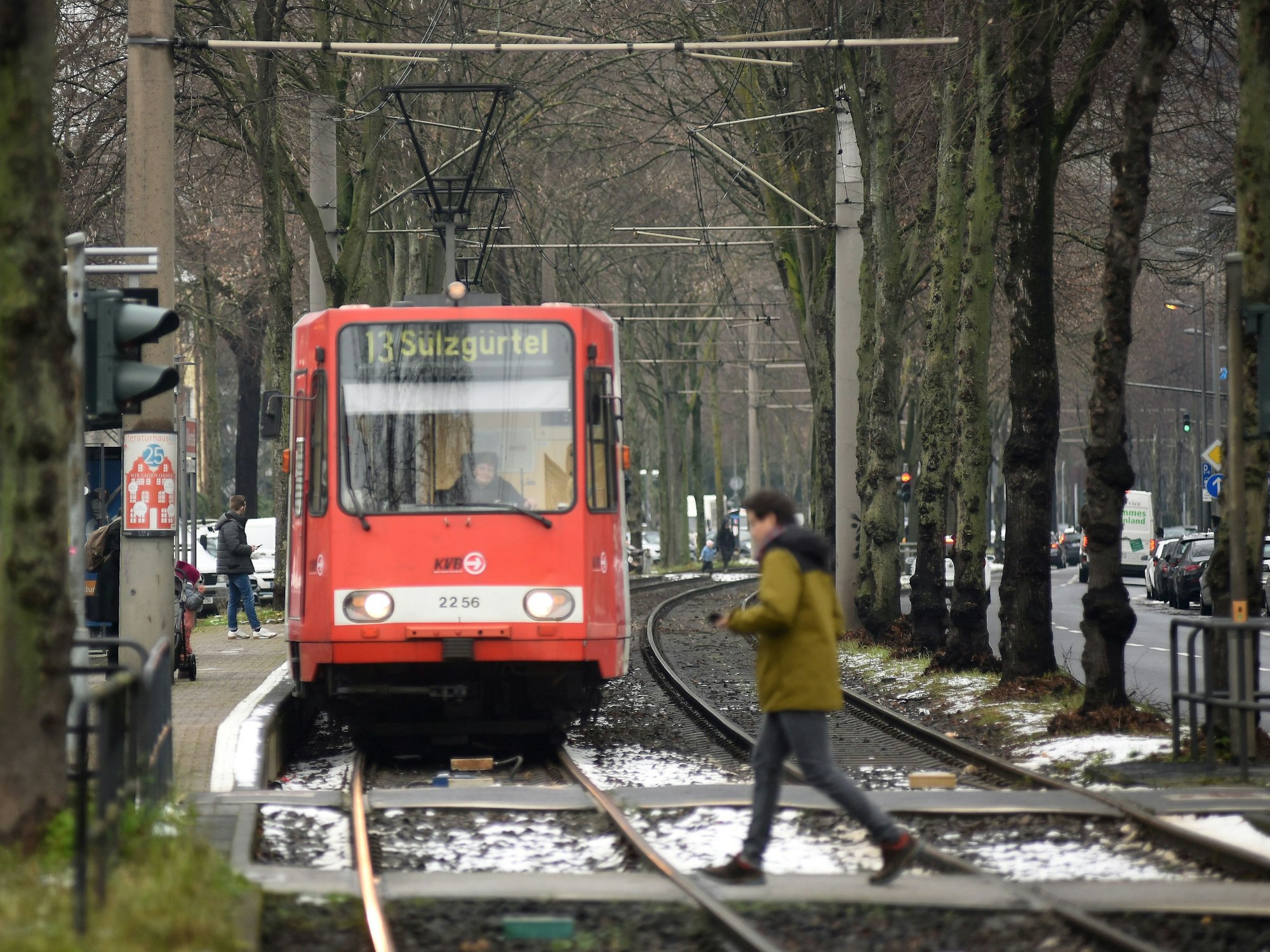 Bahn der KVB-Linie 13 fährt auf die Kamera zu. Im Vordergrund ist ein Mann zu sehen, der die Straße überquert.