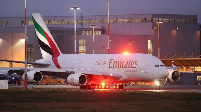 Ein Airbus A380 der arabischen Fluggesellschaft Emirates rollt zur Start- und Landebahn. Er wird von mehreren Lichtern beleuchtet.