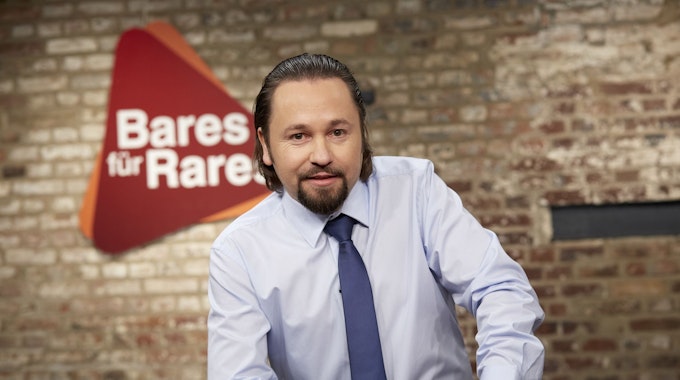Wolfgang Pauritsch lächelnd vor dem Logo der ZDF-Trödelshow „Bares für Rares“.