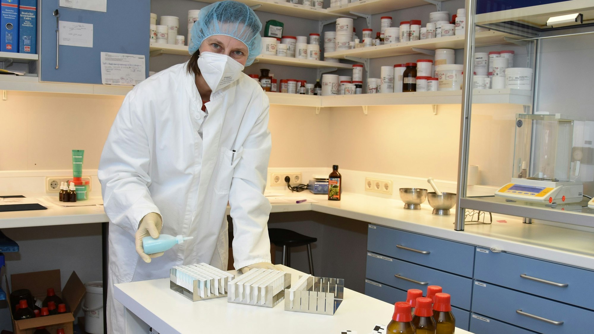 Eine Frau in weißem Kittel und mit Mundschutz stellt in einem Labor die Arzneimittel her.