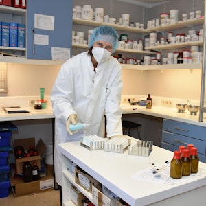 Eine Frau in weißem Kittel und mit Mundschutz stellt in einem Labor die Arzneimittel her.