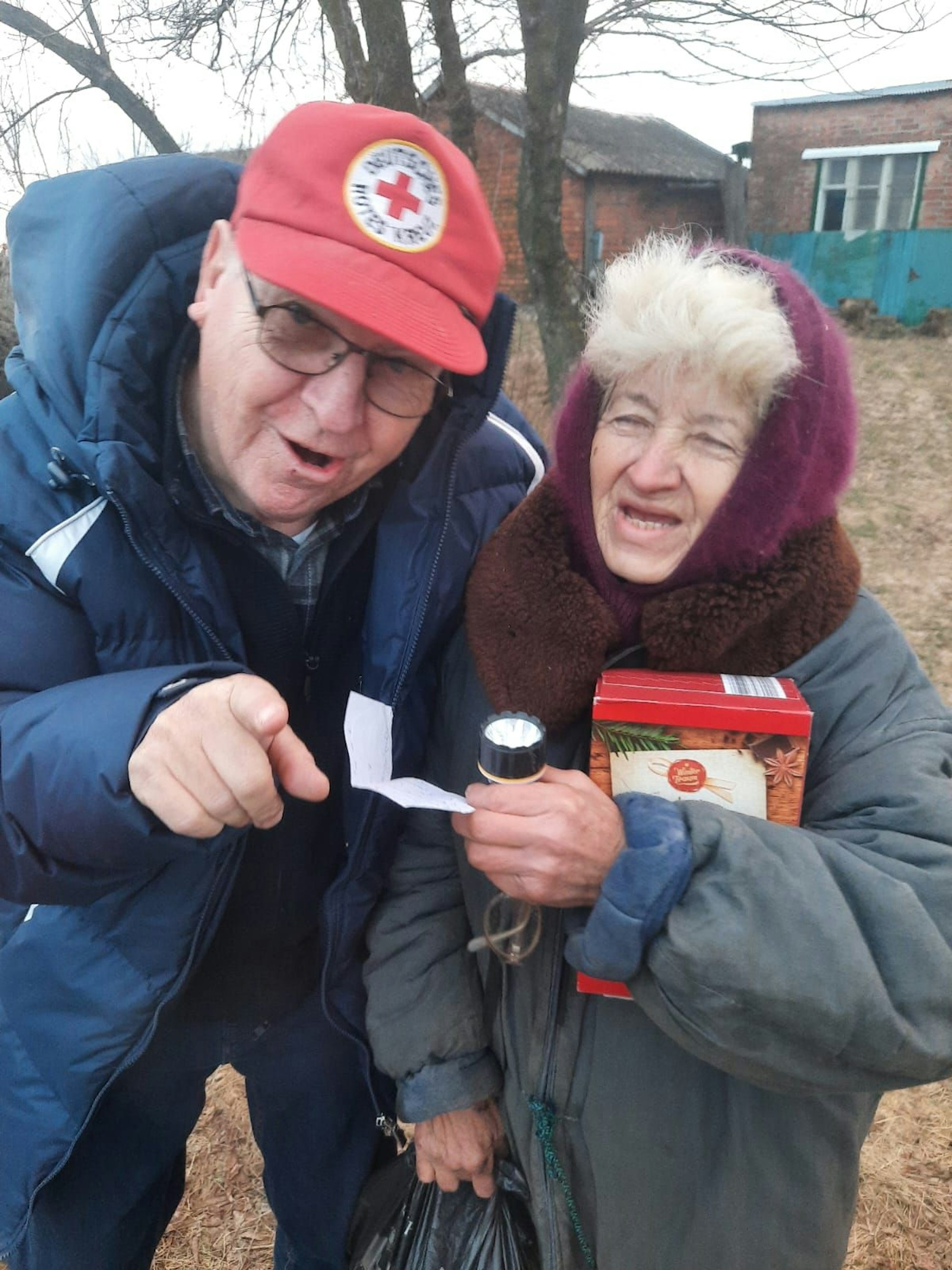 Alfred Eich von „Rheinbach Hilft“ (mit Mtze des Deutschen Roten Kreuzes) spricht mit einer Frau in einem Dorf der Ukraine, die Lebensmittel und andere Dinge zum Überleben erhalten hat.