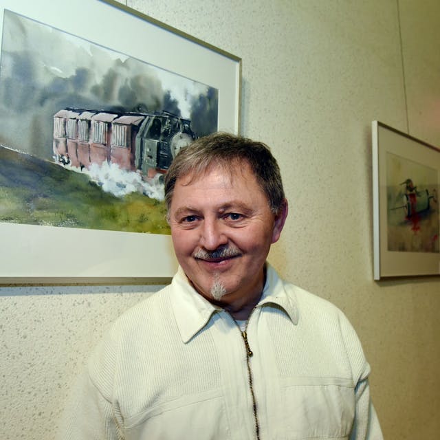 Henry Schellenberg steht vor einer Wand, an der mehrere Zeichnungen hängen.