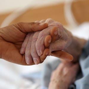 Eine Pflegerin hält die Hand einer Frau.