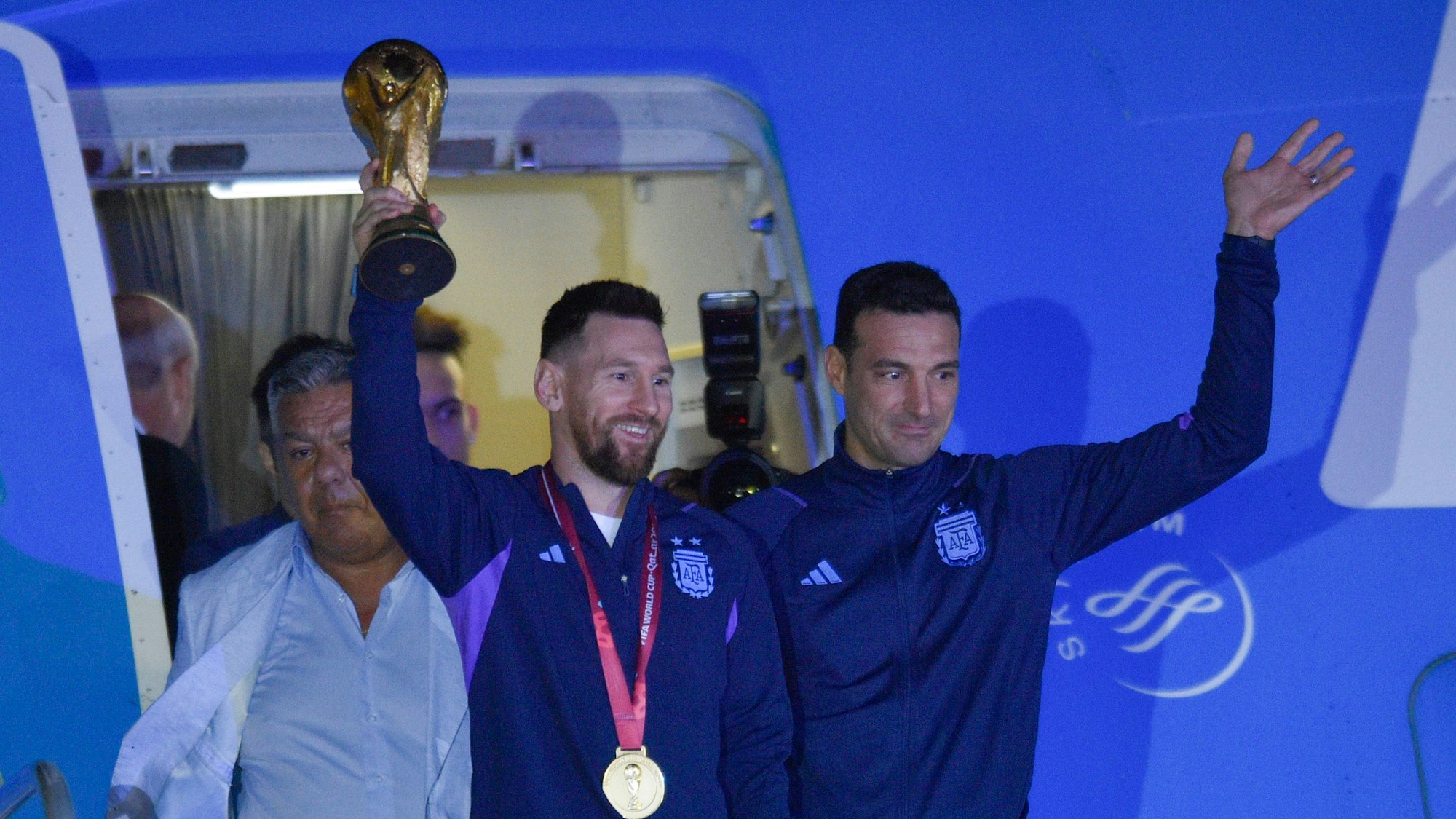 Lionel Messi (l.) hält den Weltmeisterpokal in der Hand, während er mit seinem Trainer Lionel Scaloni in Buenos Aires ankommt.