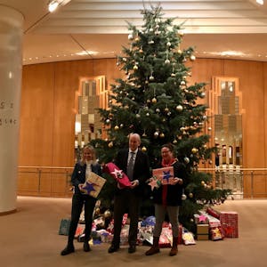 Gaby Schauenburg, Louwrens Langevoort und Gabi Schaume mit Geschenken in der Hand vor einem geschmückten Weihnachtsbaum mit Geschenken