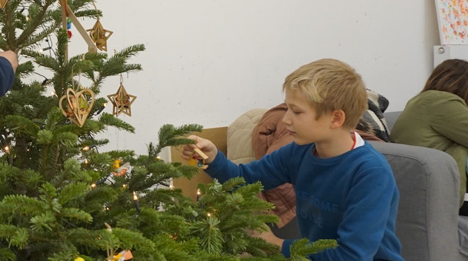 Ein Junge schmückt einen Weihnachtsbaum.