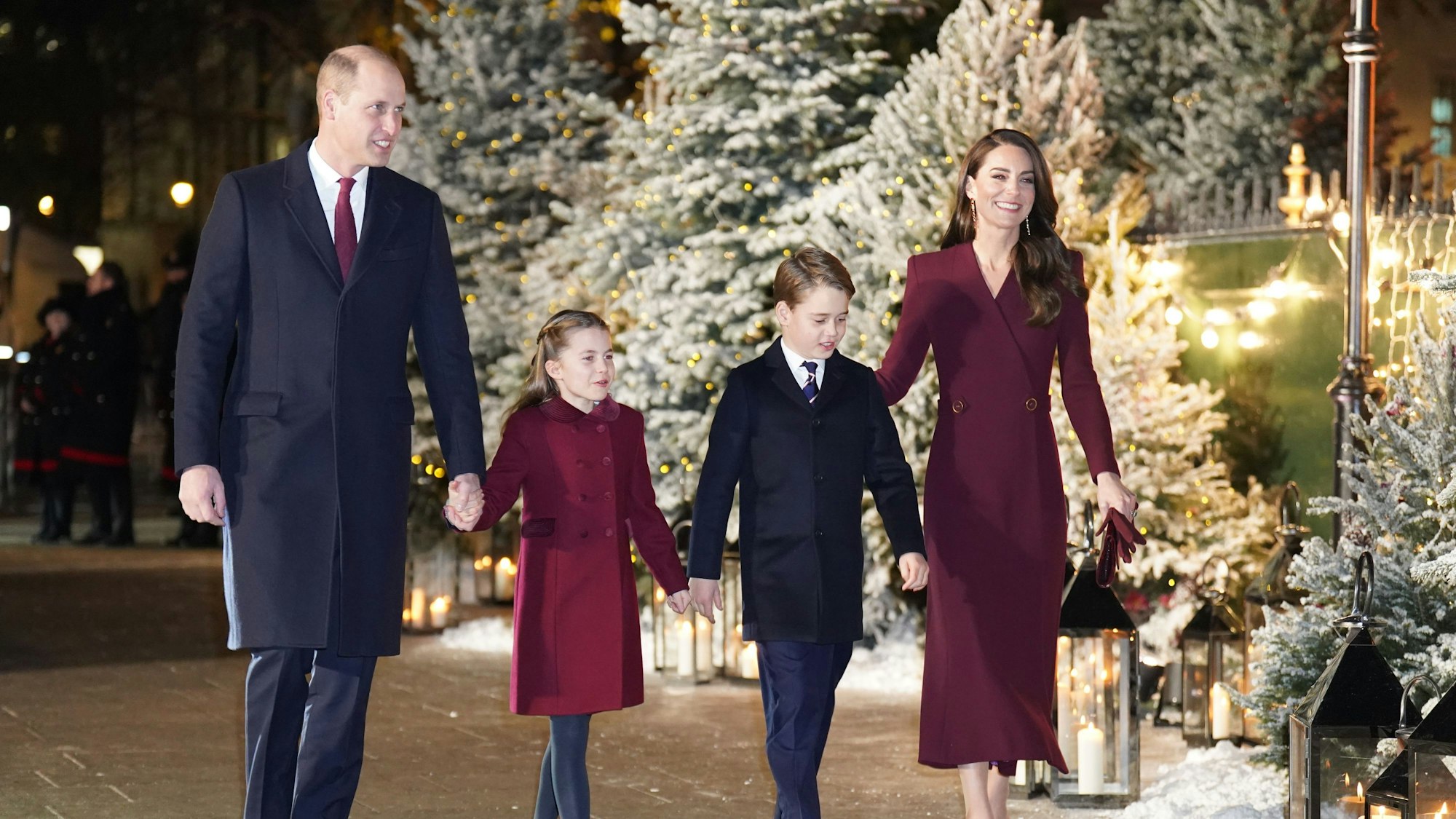 William und Kate Middleton, Prinz und Prinzessin von Wales, gehen mit ihren Kindern Prinzessin Charlotte und Prinz George. Im Hintergrund sind Weihnachtsbäume zu sehen.
