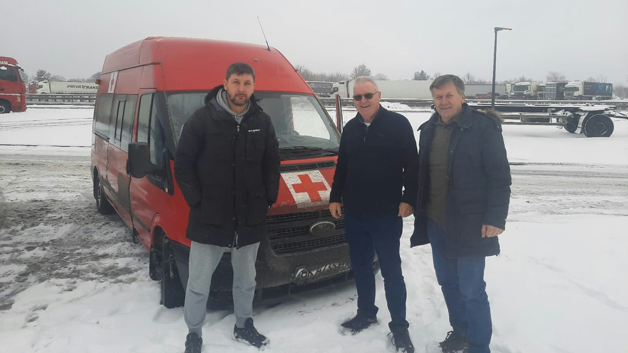 Drei Fahrer wechseln sich in der Ukraine ab. Hier stehen sie vor einem roten Lieferwagen mit Rotkreuz-Aufklebern.