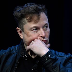 Tech-Milliardär Elon Musk sitzt mit einer Lederjacke auf einem Stuhl, er stützt den Kopf auf seinen Arm.