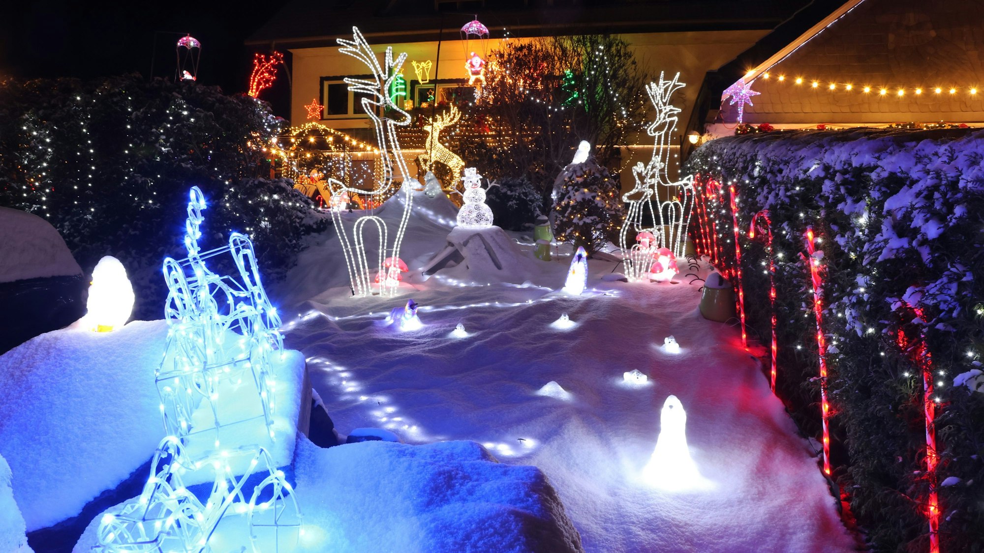 Vor einem Haus stehen auf der mit Schnee weihnachtliche Leuchtfiguren, darunter auch mehrere Rentiere.