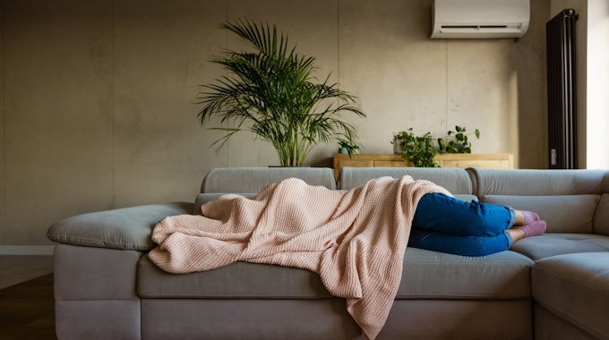 Eine junge Frau liegt auf einem Sofa und ist von einer Decke bedeckt.