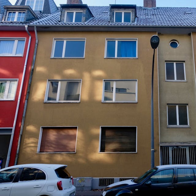 Ein vierstöckiges Wohnhaus mit brauner Fassade ist zu sehen. Davor parken Autos.