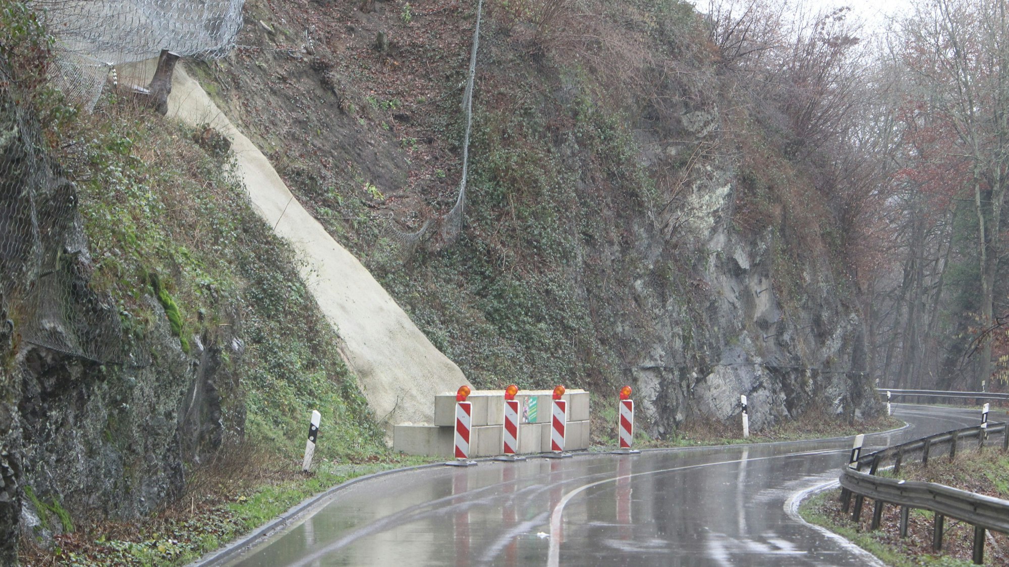 Die Landstraße 333 zwischen Hennef und Eitorf, hier im Januar 2022, nass von Regen. Am Straßenrand stehen einige Steinblöcke, die abgesperrt sind.
