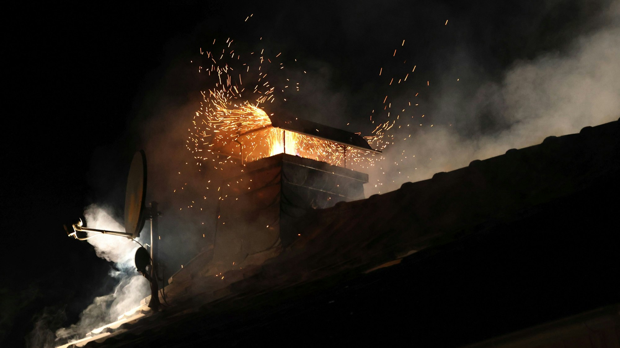 Flammen und Funken quellen aus einem Kamin auf einem Hausdach.