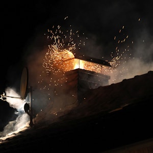 Flammen und Funken quellen aus einem Kamin auf einem Hausdach.