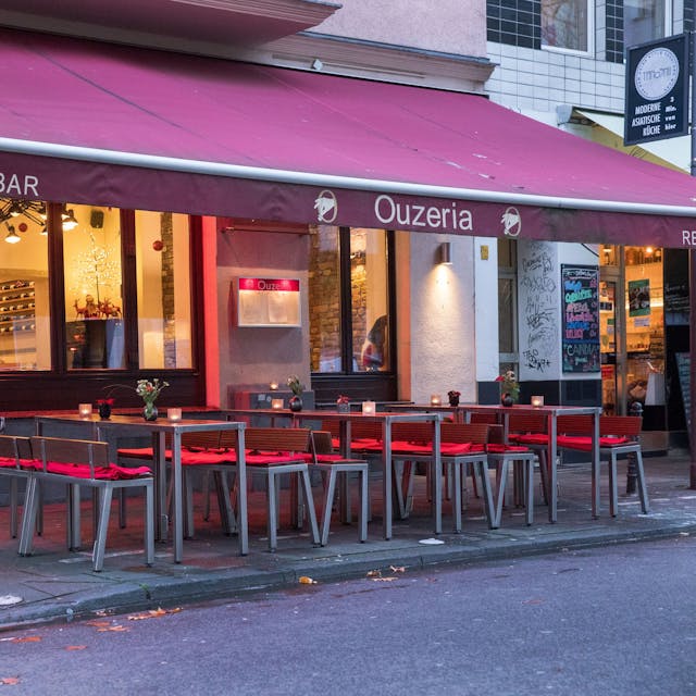 Restaurant von außen mit roter Markise über Tischen und Stühlen