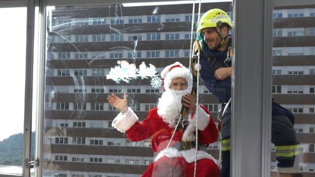 Ein als Weihnachtsmann verkleideter Mann in Spanien winkt vor einem Fenster.