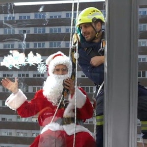 Ein als Weihnachtsmann verkleideter Mann in Spanien winkt vor einem Fenster.