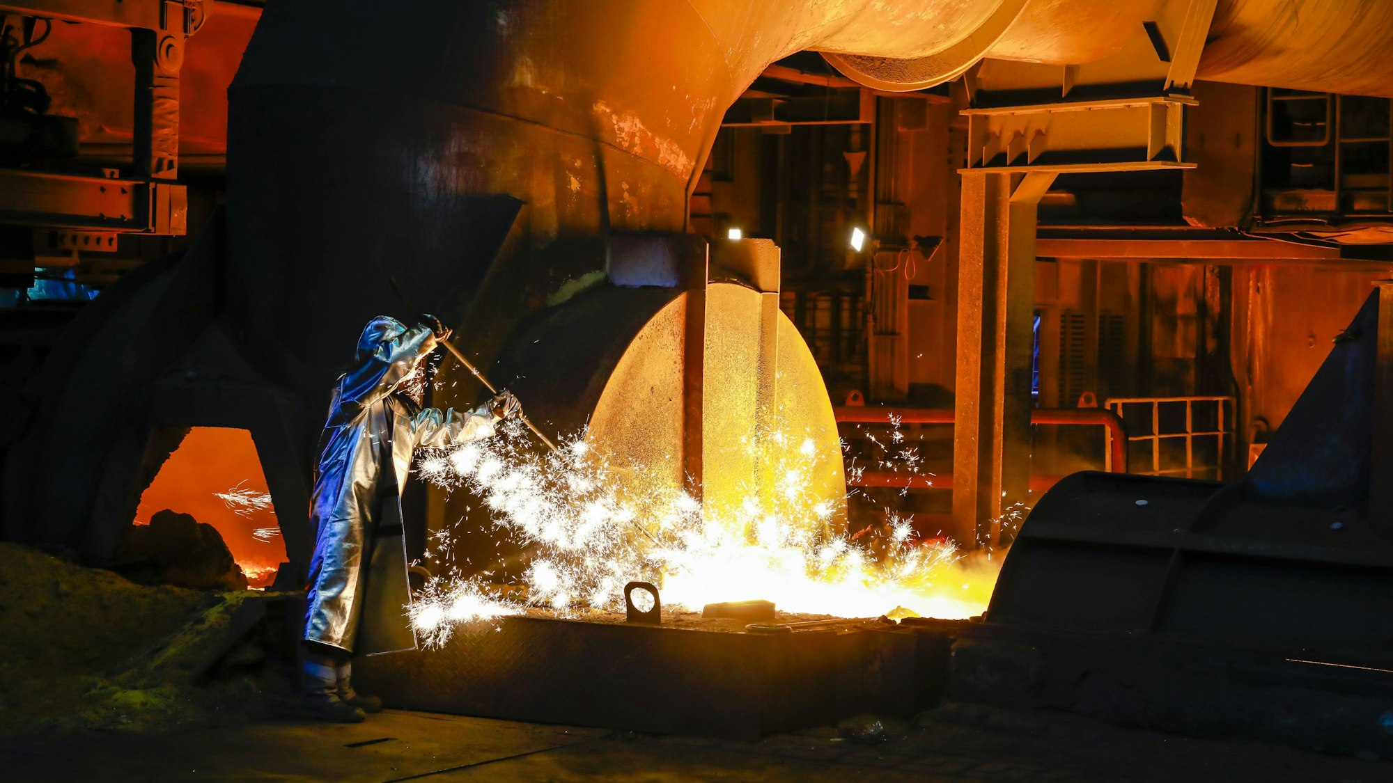 ThyssenKrupp Steel, ein Stahlarbeiter im Schutzanzug entnimmt eine 1500 Grad heisse Roheisenprobe.