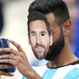 Ein Fan mit der Gesichtsmaske von Argentiniens Lionel Messi bedient sein Smartphone.
