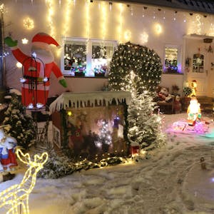 Vor einem Haus leuchten zahlreiche weihnachtliche Figuren und Lichterketten in bunten Farben. Ein aufblasbarer Nikolaus winkt.