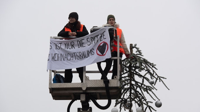 „Es ist nur die Spitze des Weihnachtsbaums“ steht auf dem Transparent der Aktivisten der „Letzten Generation“. Zwei Aktivisten der Umweltschutzgruppe fuhren mit einem Hubwagen vor dem Tannenbaum auf dem Pariser Platz am Brandenburger Tor.