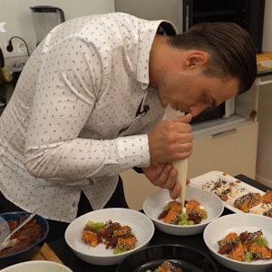 „Das perfekte Dinner“-Kandidat Tomek verziert seine Lachs-Vorspeise in der Küche.
