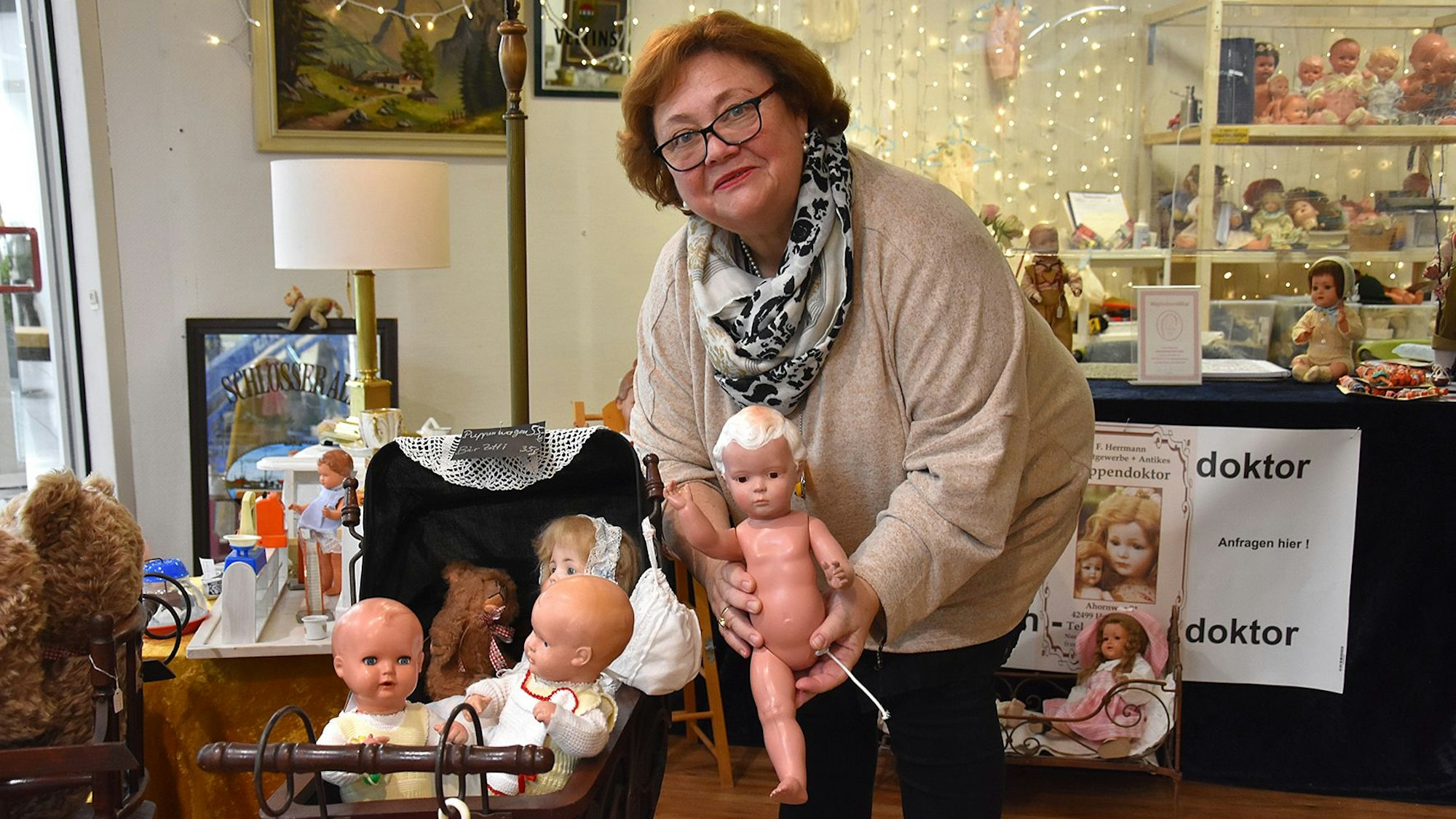 Daniela Herrmann steht in ihrer Puppenwerkstatt und hält eine kaputte Puppe ohne Bein in die Kamera.