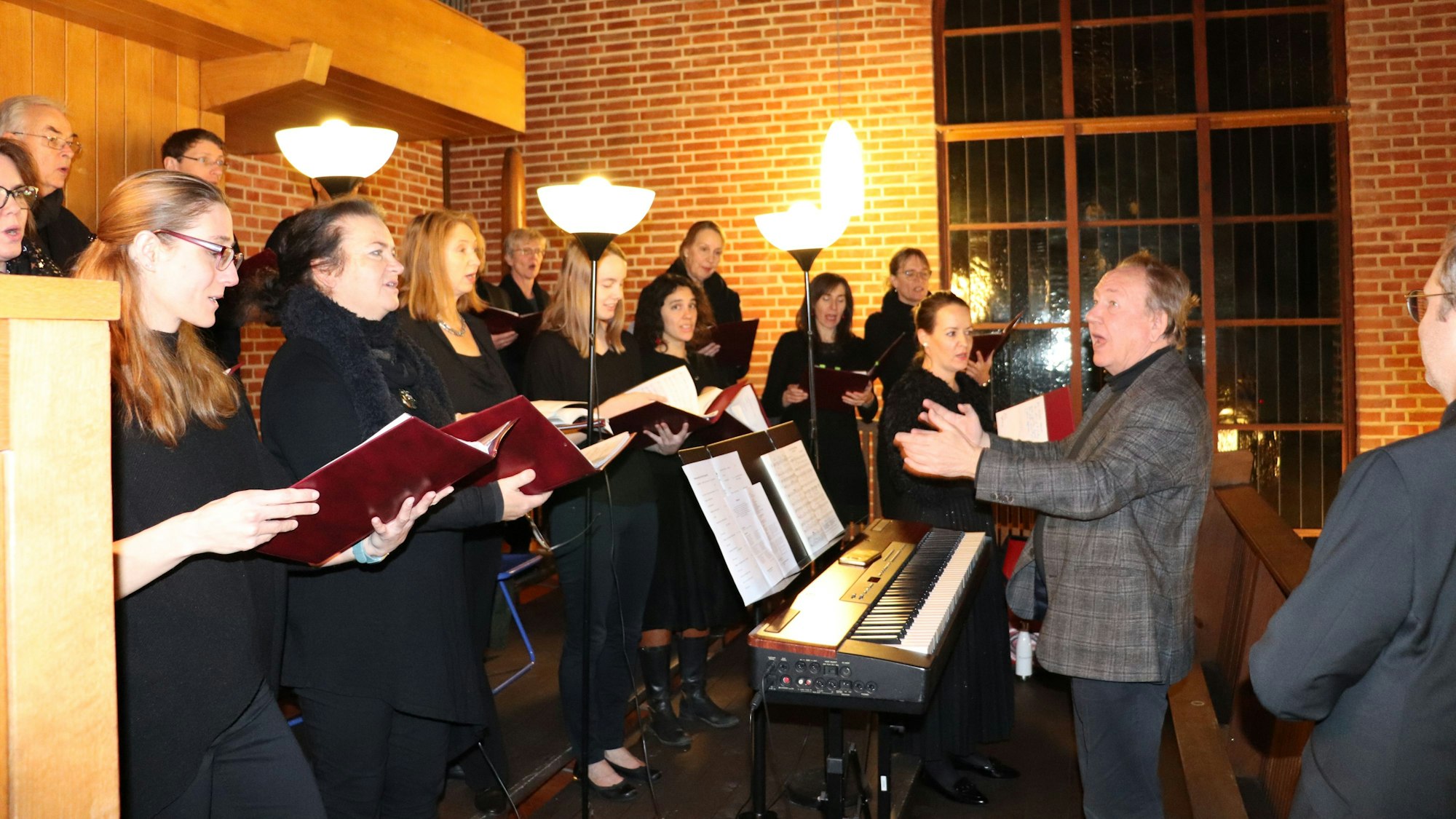 Sängerinnen mit Noten in der Hand und ein Chorleiter stehen im Halbkreis in einer Kirche.
