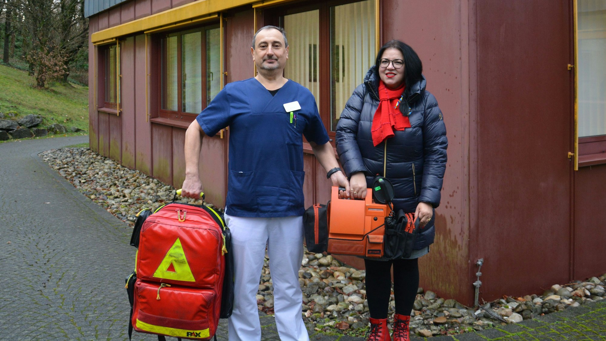 Igor Prudkov und Valentyna Butulay zeigen weitere medizinische Hilfsmittel, die dank Spenden ins Krankenhaus nach Charkiw geschickt werden können. Sie halten einen Notfallrucksack und einen Defibrillator in den Händen.