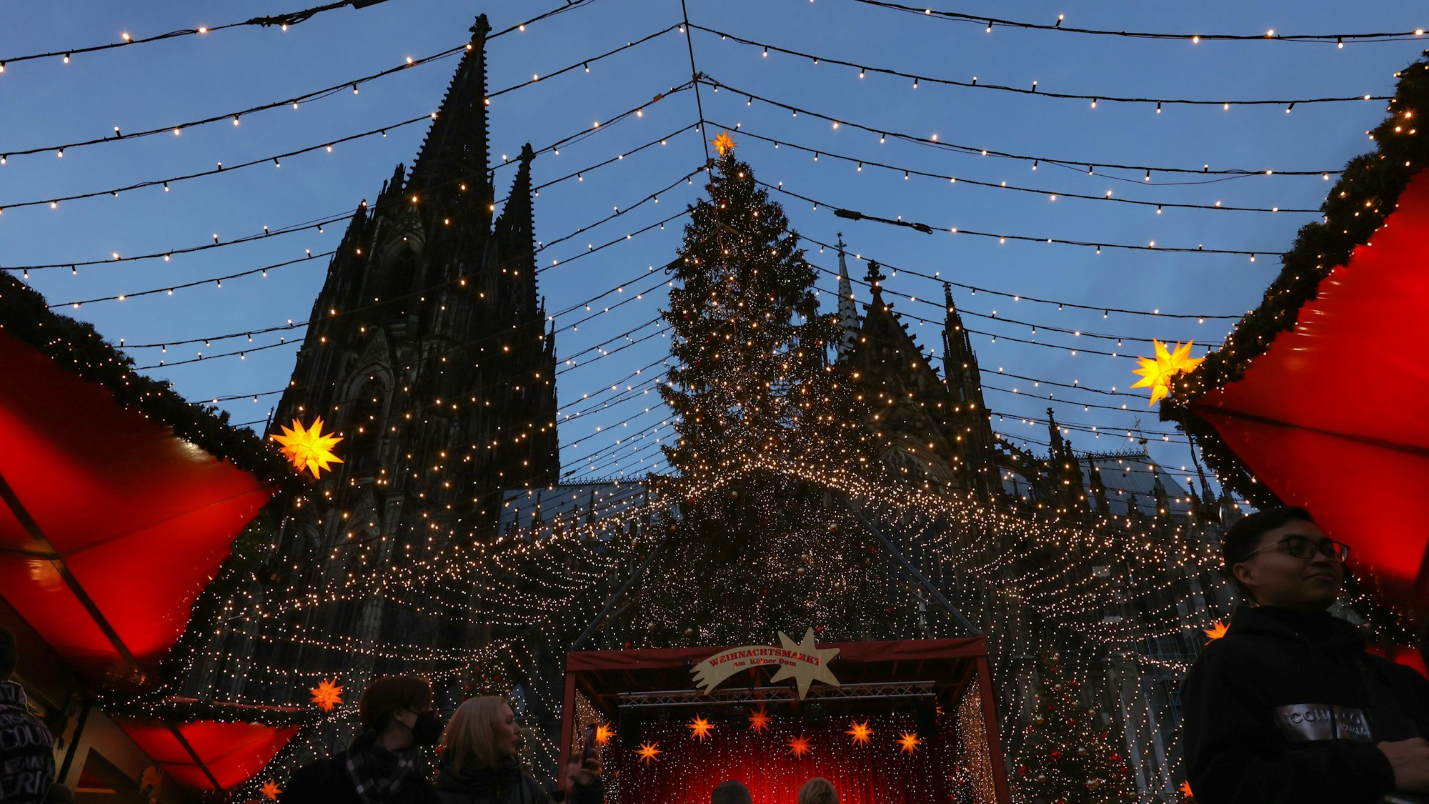 Die Spitzen des Kölner Dom erheben sich hinter dem Weihnachtsmarkt auf dem Roncalliplatz.



