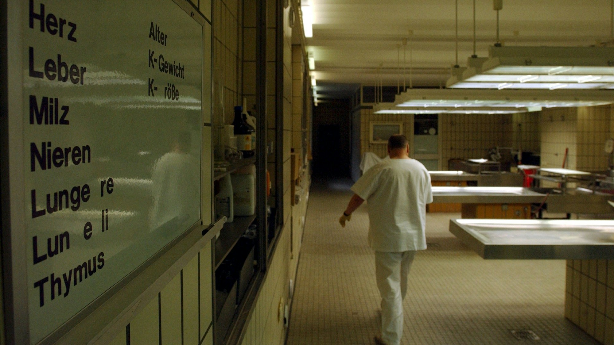 Ein Mann in weißen Klamotten geht an metallenen Tischen in der Rechtsmedizin Köln vorbei.