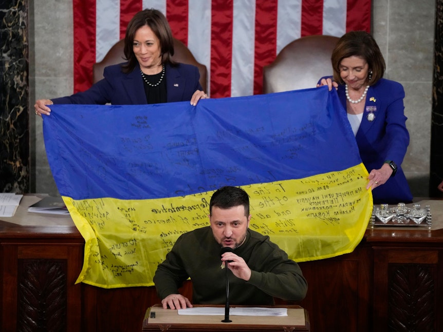 Wolodymyr Selensky spricht am 21. Dezember 2022 vor einer überreichten ukrainischen Flagge im US-Kongress. Hinter ihm Kamala Harris (l.), Vizepräsidentin der USA, und Nancy Pelosi, zu dem Zeitpunkt noch Sprecherin des Repräsentantenhauses.