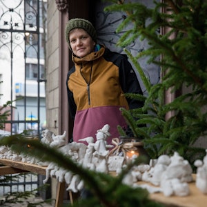 Monika Lioba Lang steht neben einem Tannenbaum hinter Krippenfiguren aus Ton.