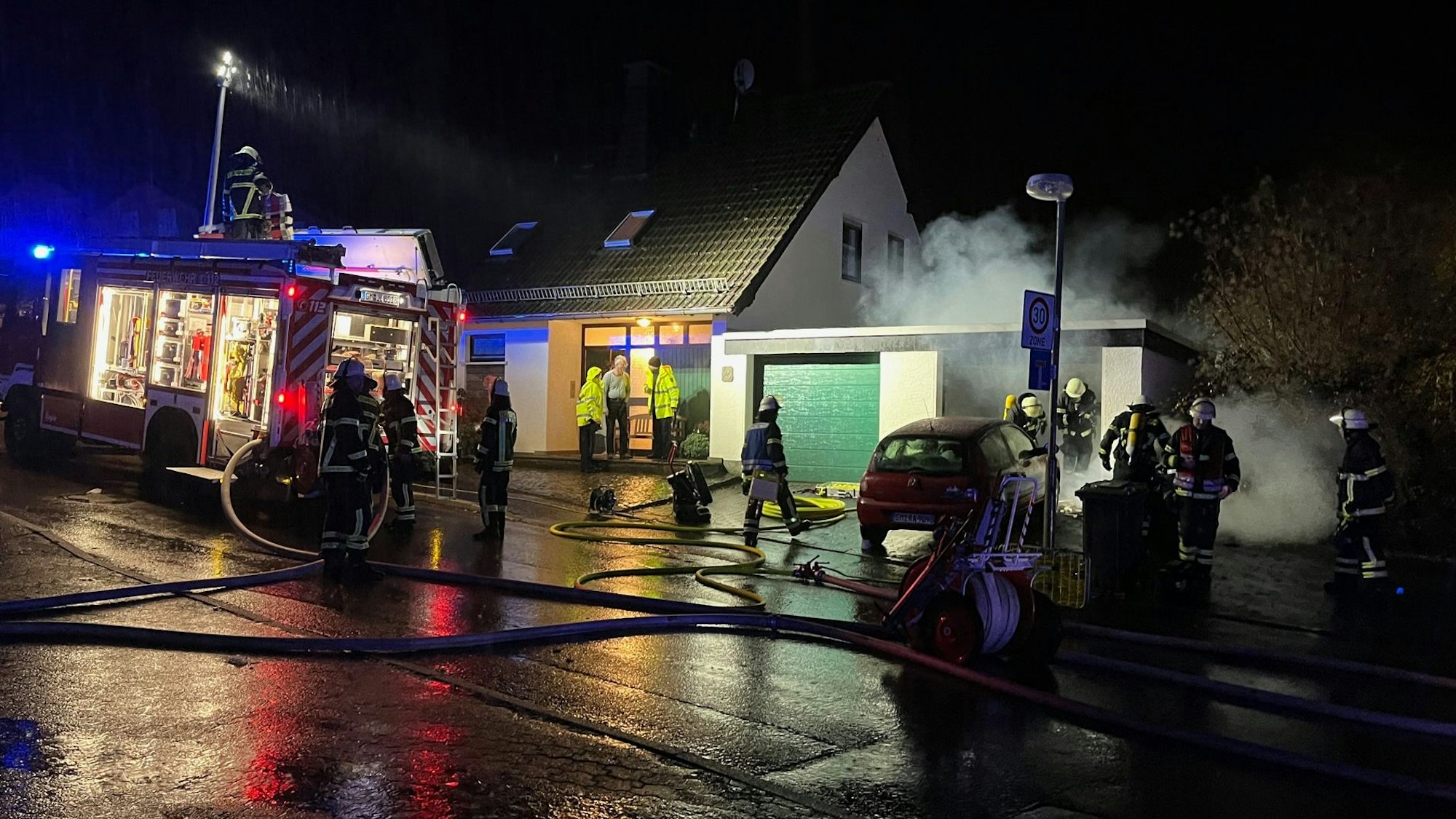 Feuerwehrleute stehen vor einer Garage in Lindlar, aus der Rauch dringt.