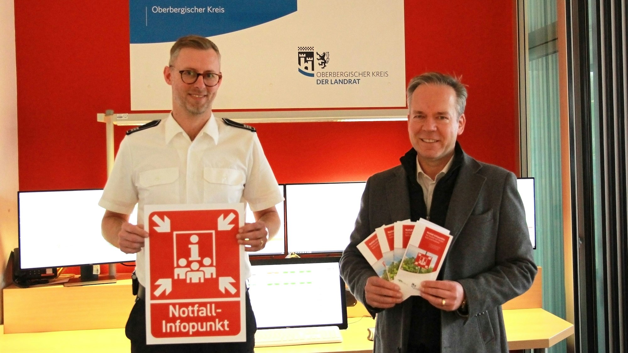 Leitstellen-Chef Julian Seeger (l.) und Kreisdirektor Klaus Grootens halten ein knallrote Symbol in der Hand, das bei einem Stromausfall auf Notfallpunkte hinweisen soll.