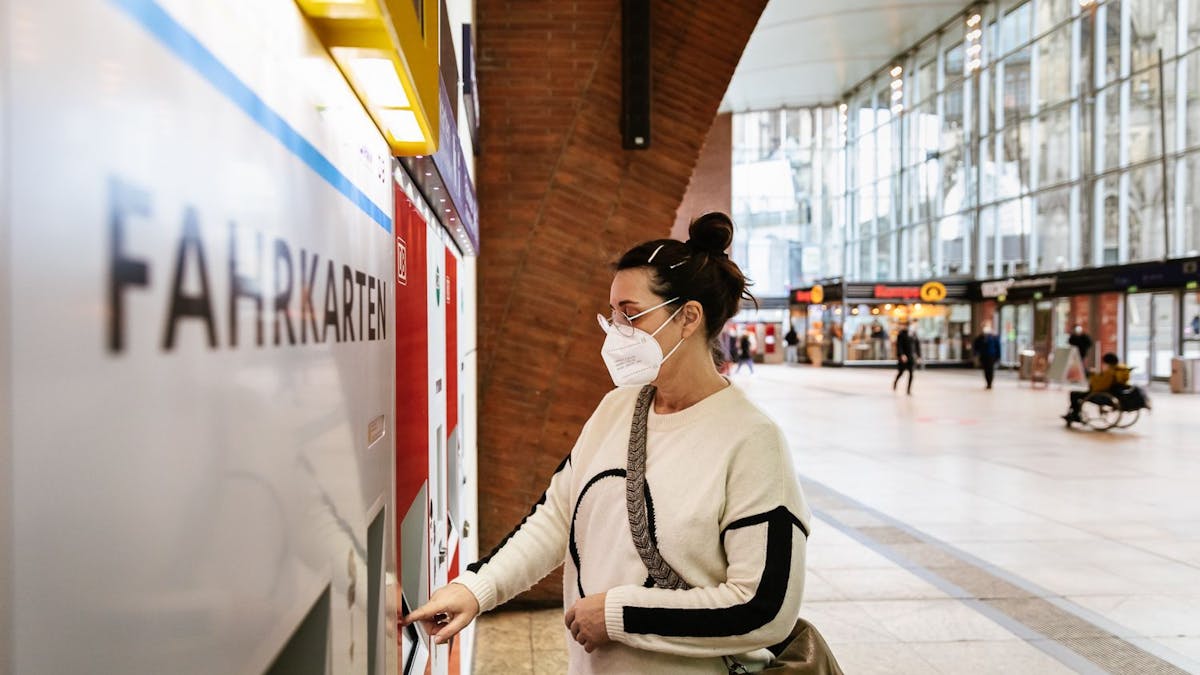 Eine Frau mit Maske zieht sich im Kölner Hauptbahnhof ein Ticket aus einem VRS-Automaten.