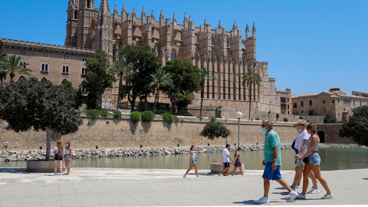 Touristen und Touristinnen gehen vor der Kathedrale von Palma auf Mallorca entlang. Die Aufnahme dient als Symbolfoto.