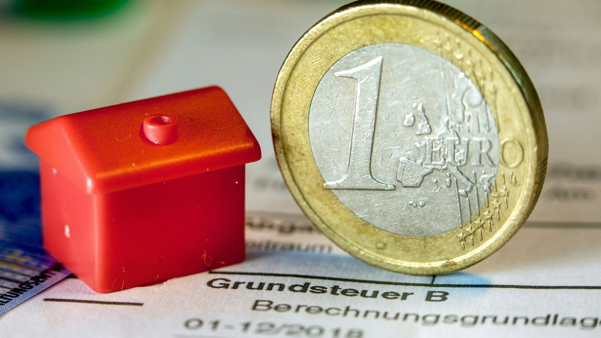 Das Foto zeigt eine Euro-Geldmünze sowie ein Spielzeughaus stehen auf einem Abgabenbescheid für die Entrichtung der Grundsteuer im September 2019.