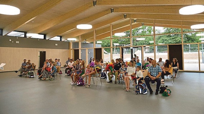 In einem großen Raum in der neu gebauten Grundschule in Neschen sitzen viele Menschen.