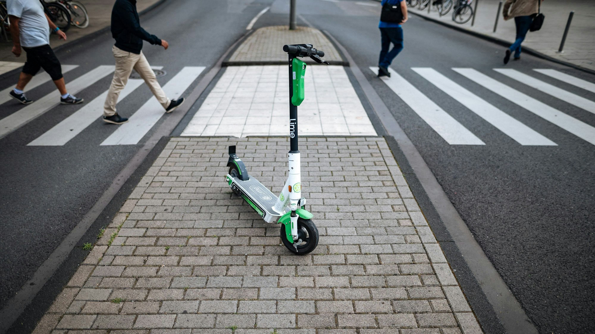 Ein E-Scooter des Unternehmens Lime steht vor einem Zebrastreifen in der Kölner Innenstadt.