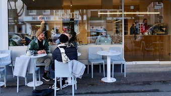Drei junge Männer sitzen an einem Tisch vor dem Café und unterhalten sich.